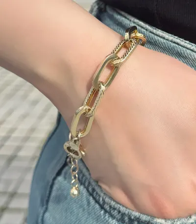 Close-up of the same bracelet on the wrist: long flat links, some smooth and some engraved with fine diagonal lines, and the round clasp with its short extension chain.